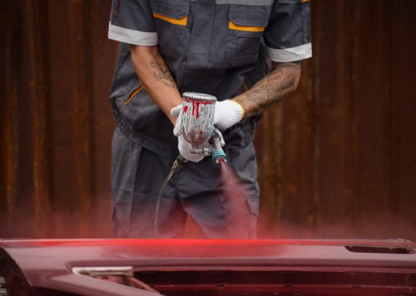 работник распыляет порошковую краску из пистолета на автомобиль